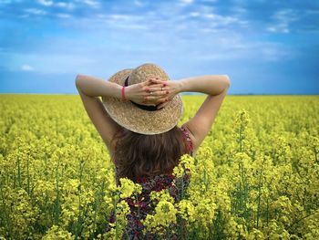 Rear view of woman wearing dress and hat in a field of canola flowers on a cloudy day