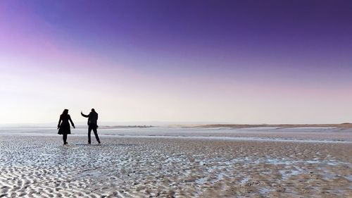 Silhouette man and woman at beach against clear purple sky