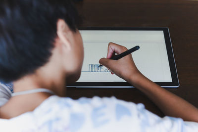 Closeup young school boy with stylus pen writing on digital notepad.