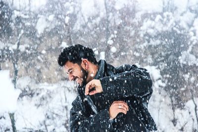 Playful man standing against trees during snowfall