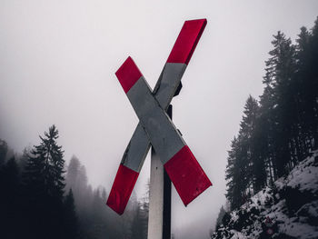 Cross shape information sign against snowcapped mountain during foggy weather