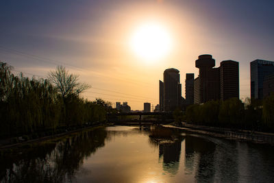 Scenic view of river by buildings against sky during sunset