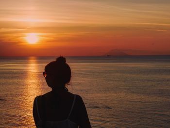 Rear view of woman against sea and sky during sunset