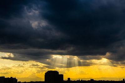 Silhouette buildings against dramatic sky during sunset