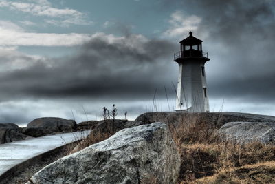 Lighthouse on rock by building against sky