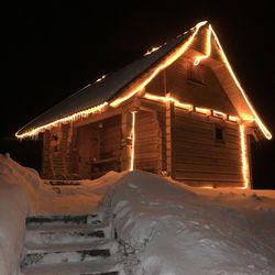 Illuminated building covered with snow against sky at night