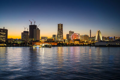 Illuminated buildings by sea against sky in city