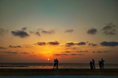 People at beach against sky during sunset