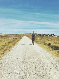 Rear view of man walking on road against sky