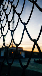 Close-up of chainlink fence against sky during sunset