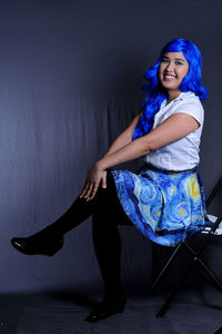 Portrait of a smiling young woman sitting against wall