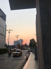 Traffic on city street by buildings against sky during sunset