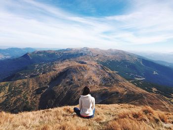 Rear view of woman sitting on landscape against sky