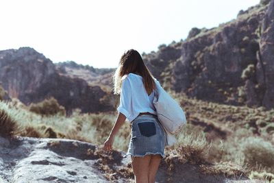 Rear view of woman walking on mountain against clear sky