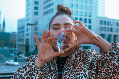 Close-up of woman with mouth open reflecting on crystal against buildings in city