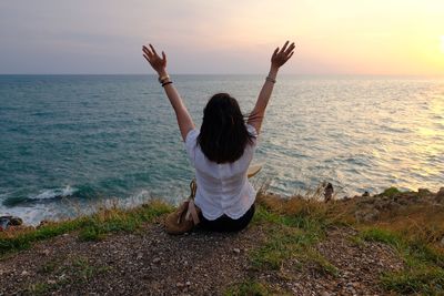 Rear view of woman at sea shore against sky during sunset