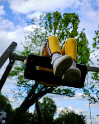 Low section of girl sitting on swing against sky