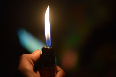 Close-up of human hand holding lit cigarette lighter in darkroom