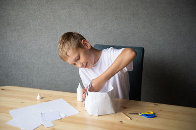 The boy cuts out details from paper. glue the parts together with glue.