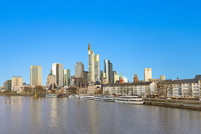 Buildings by river against clear blue sky