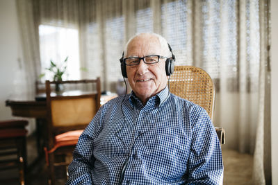 Portrait of smiling senior man hearing music with headphones at home