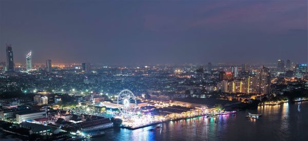 Illuminated city by river against sky at night