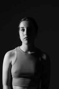 Portrait of young woman standing against black background