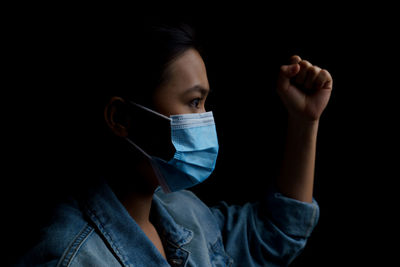 Close-up of young woman wearing flu mask standing against black background