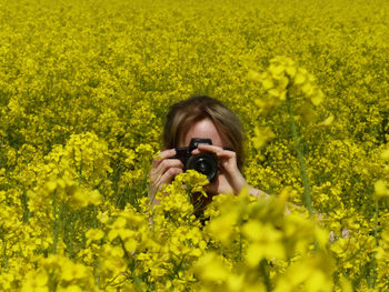 Portrait of young woman photographing with yellow flowers