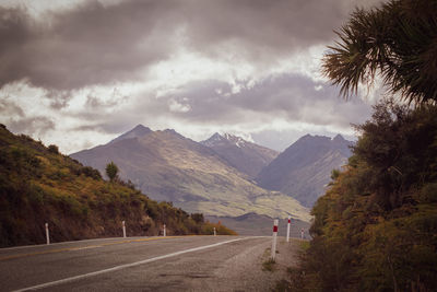 Road amidst trees and mountains against sky