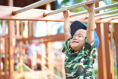 Cute boy hanging from monkey bar at playground