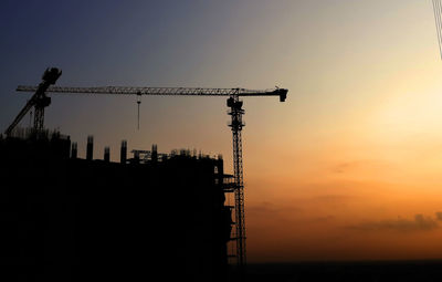 Silhouette cranes at construction site against sky during sunset