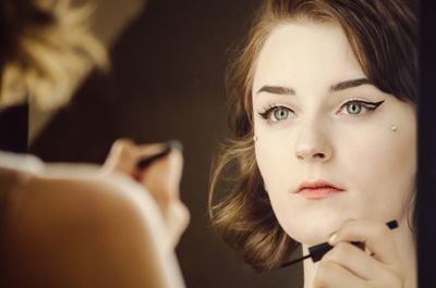 Reflection of young woman applying eyeliner in mirror