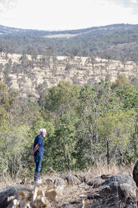 Side view of man standing on land against trees