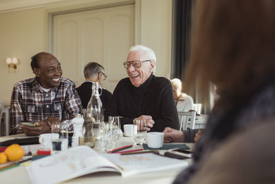 Cheerful elderly male friends talking at table in retirement home