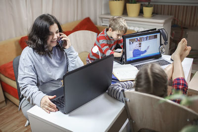 High angle view of mother talking over phone by siblings studying over laptop at home