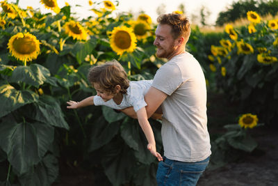 Father with little baby son in sunflowers field during golden hour. 