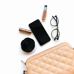 High angle view of purse with smart phone and eyeglasses against white background