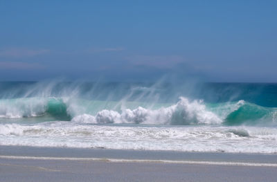 Waves splashing on shore against sky