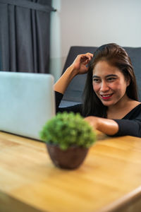 Portrait of smiling woman using phone while sitting on table