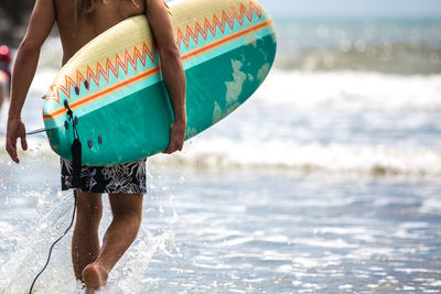 Low section of man carrying surfboard while walking at beach