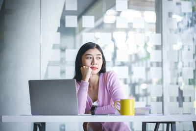 Portrait of young woman using phone while sitting on table