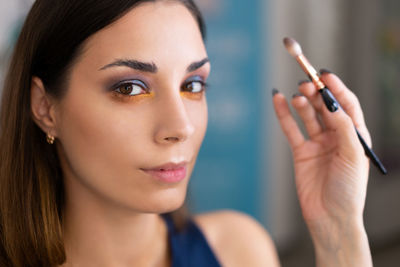 Cropped hand of beautician holding make-up brush by woman face