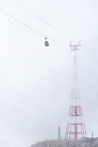 A cable car, mountain gondola suspended on a rope disappearing in fog. the red-white steel pylon.