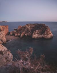 Scenic view of rocks by sea against sky