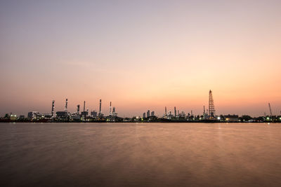 Factory by sea against sky during sunset