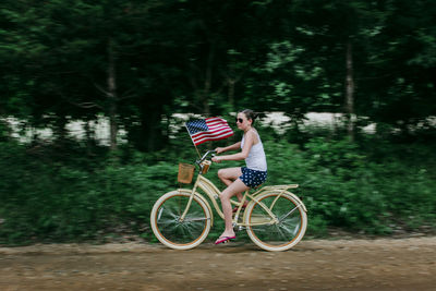 Girl riding her bike with an american flag on a rural dirt road