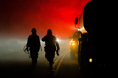 Silhouette firefighters walking on road against sky at night