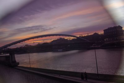 Bridge over river in city against sky at sunset