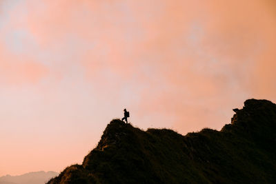 Low angle view of silhouette man standing on cliff against sky during sunset